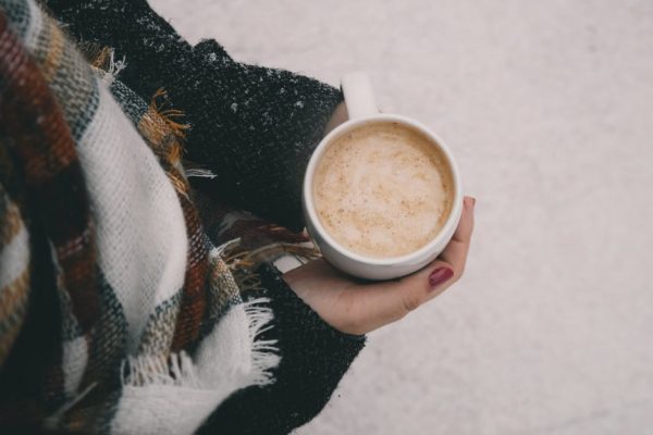 Hands holding a mug of coffee with a snowy background