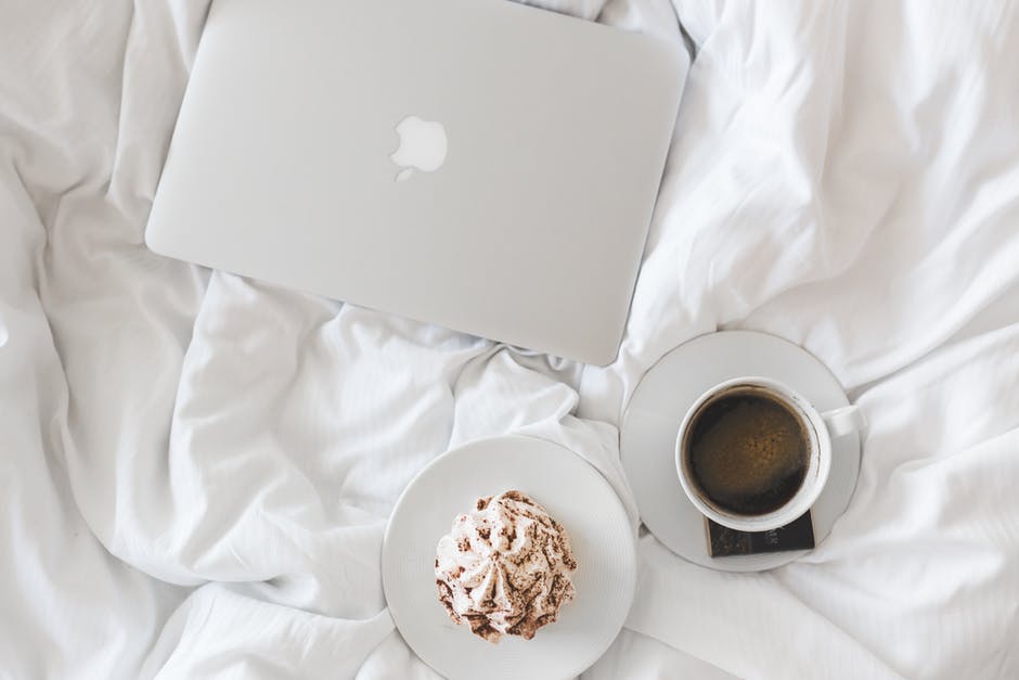 A laptop, muffin and cup of coffee on bedding
