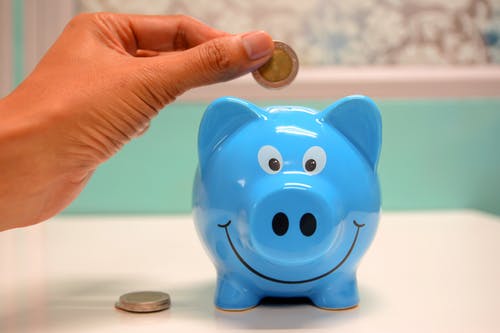 a hand putting a coin in a blue piggy bank