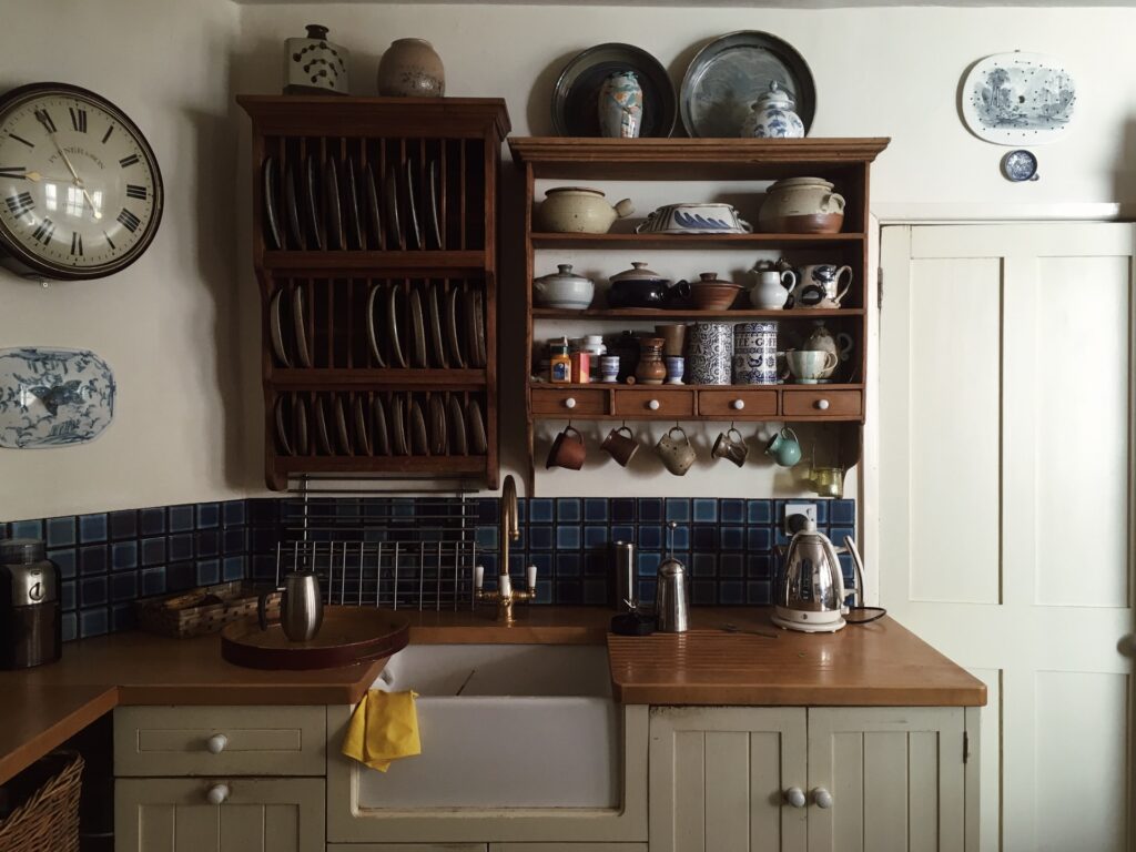 a small kitchen sink with shelves above it storing dishware and mugs
